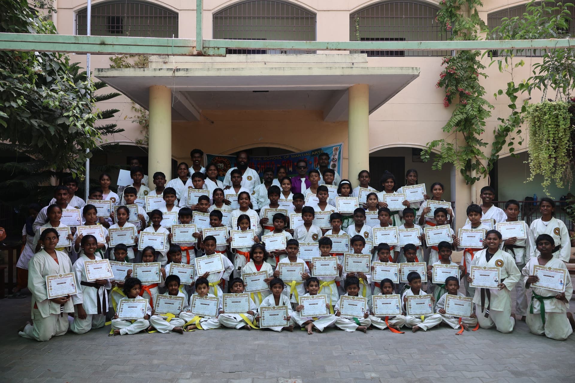 Group of karate students in white gi displaying various colored belts after successful grading exam