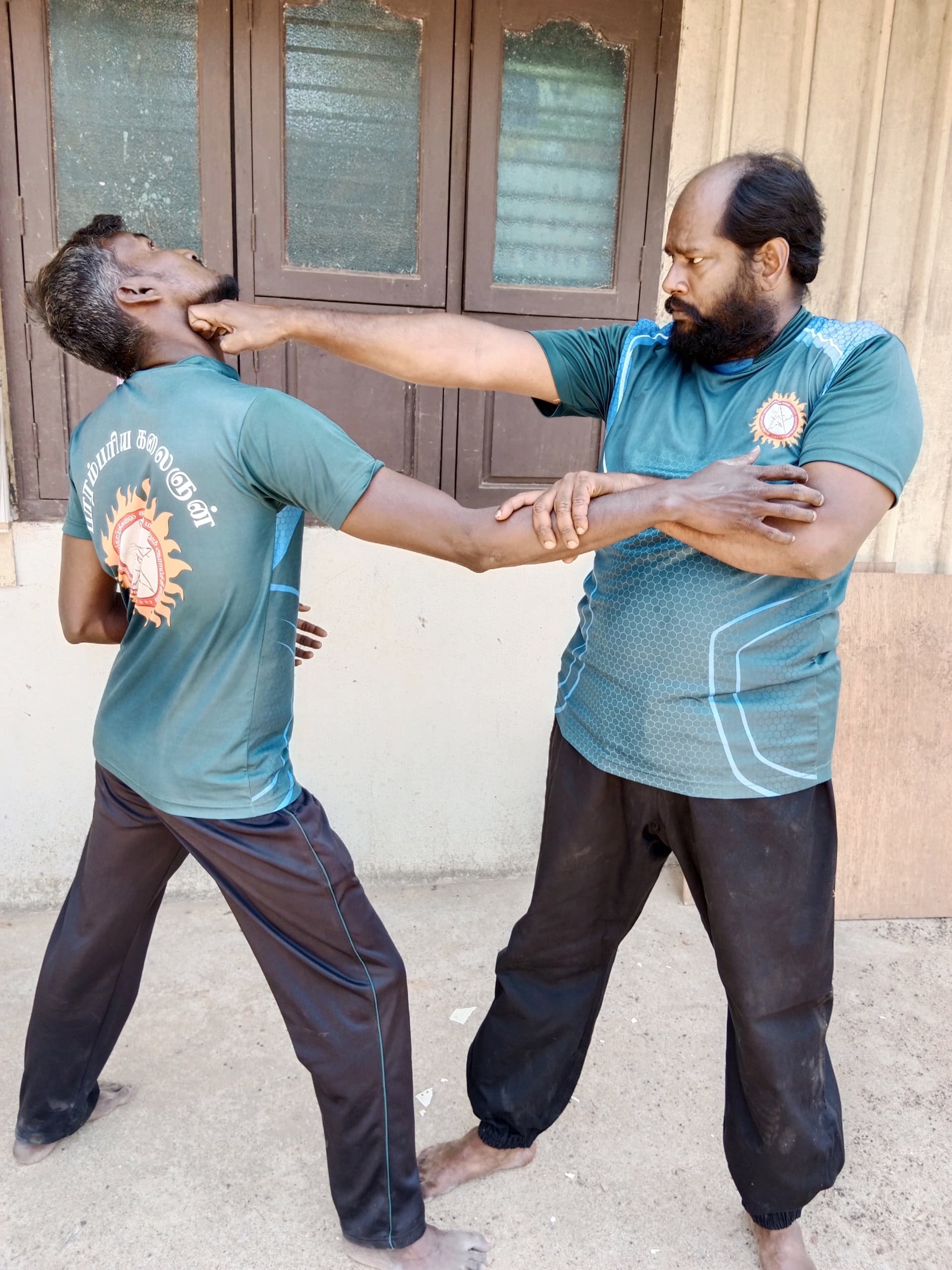 Large group of silambam students in white uniform arranged in traditional training formation with wooden staffs
